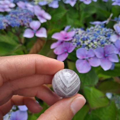 Dumi's Crystals | Chevron Amethyst Mini Sphere (20mm) | A close-up view of a captivating Chevron Amethyst Mini Sphere, showcasing its vibrant purple hues with distinct white chevron markings. This 20mm sphere is believed to promote balance, clarity, spiritual growth, and protection. It's also thought to enhance intuition and create a shield against negativity.