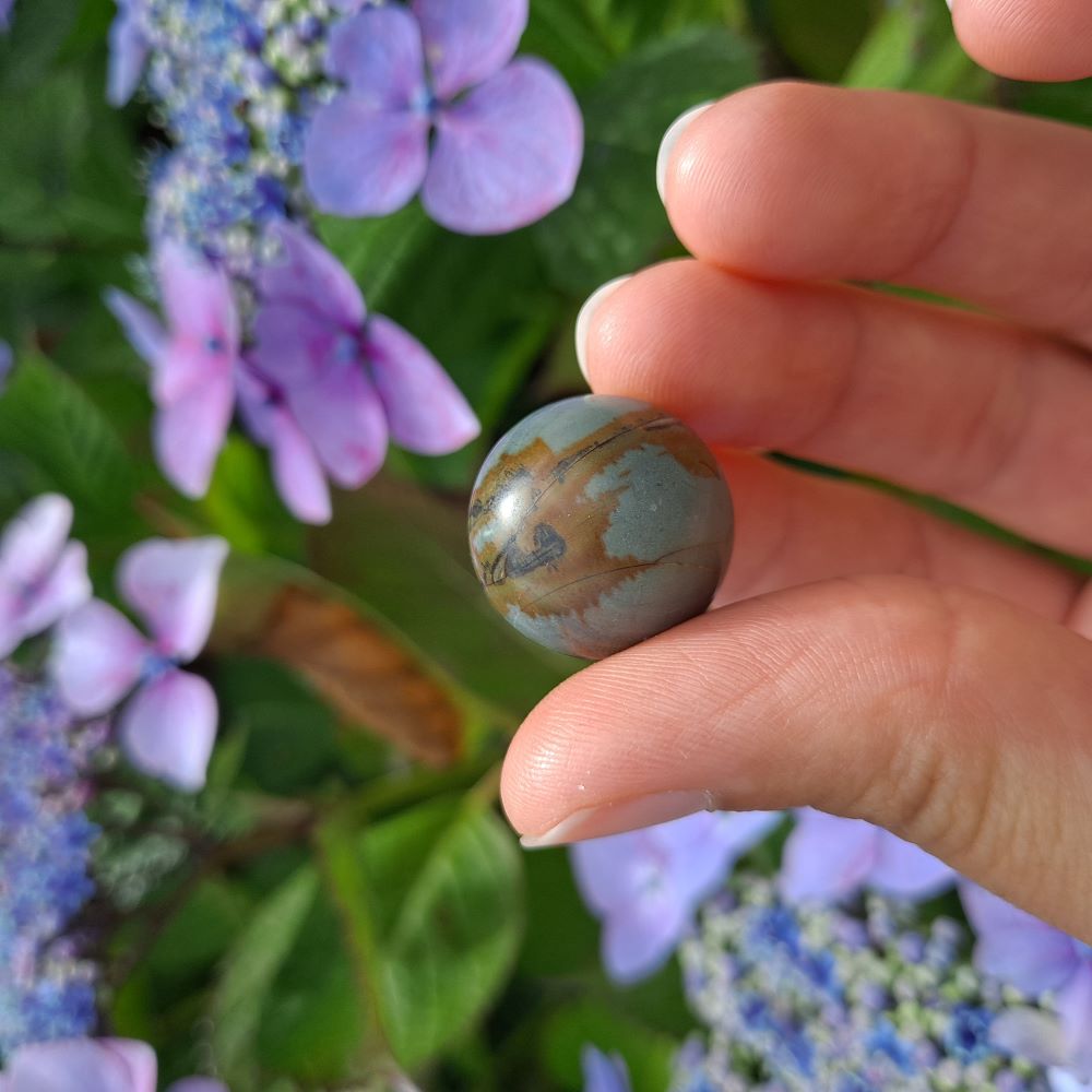 Dumi's Crystals | Frosted Polychrome Jasper Mini Sphere (20mm) | A close-up view of a captivating Frosted Polychrome Jasper Mini Sphere, showcasing its beautiful frosted finish and unique blend of earthy tones. This 20mm sphere is believed to promote peace, balance, and inner strength. It's also thought to be a grounding stone, reducing stress and anxiety.